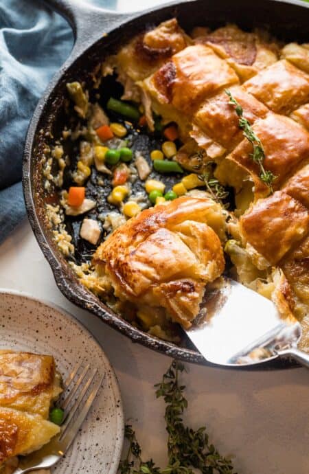 turkey pot pie with puff pastry in a cast iron skillet being scooped out