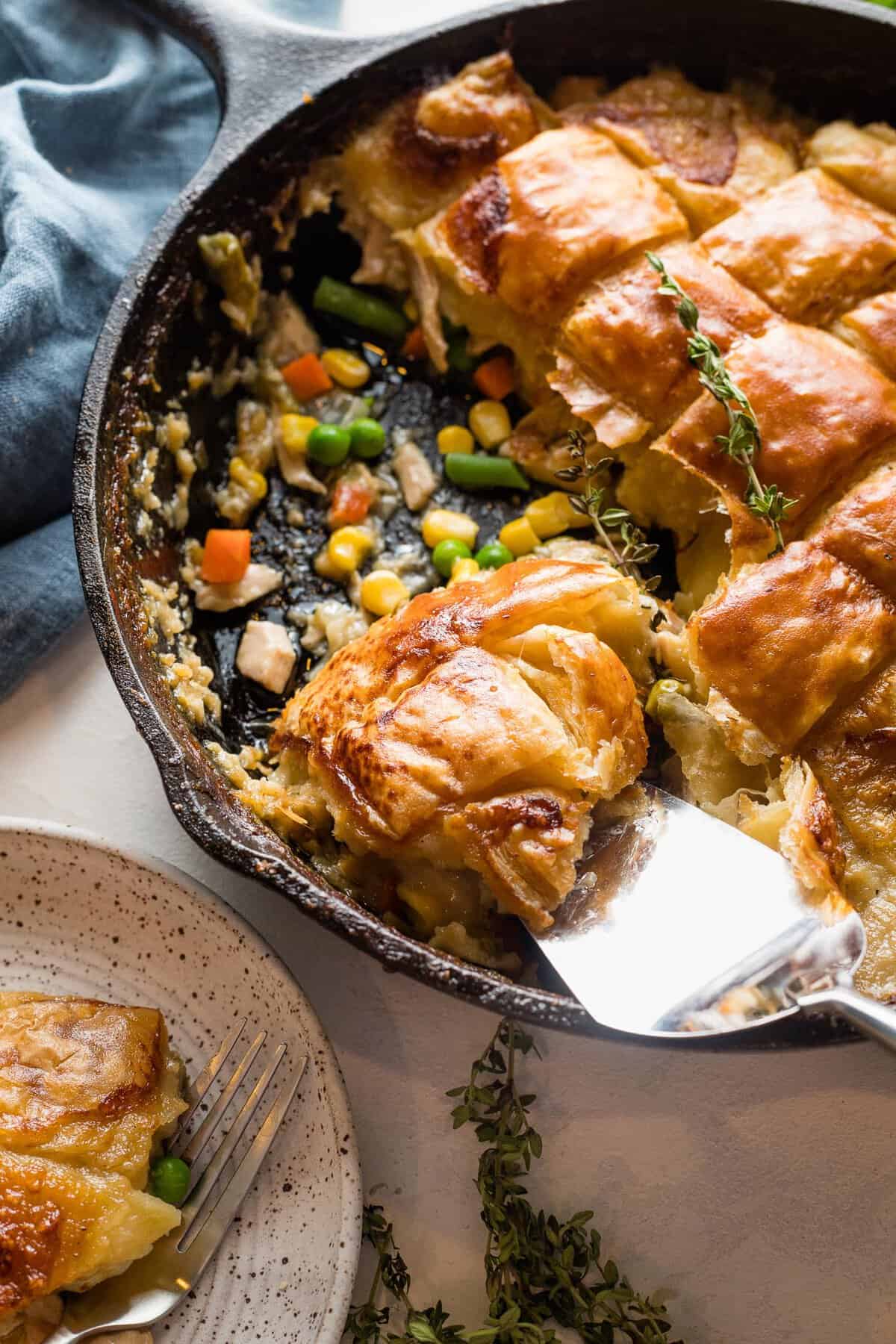 turkey pot pie with puff pastry in a cast iron skillet being scooped out