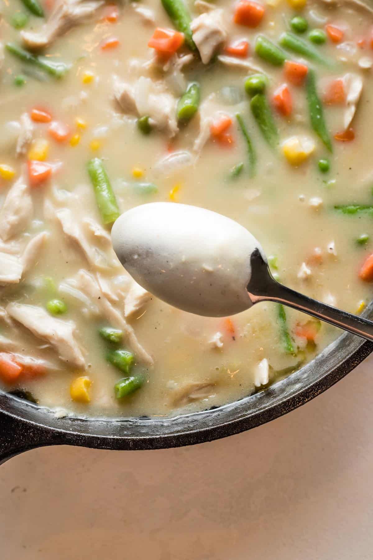 A spoon showing how thick the filling of turkey pot pie needs to be after simmering.