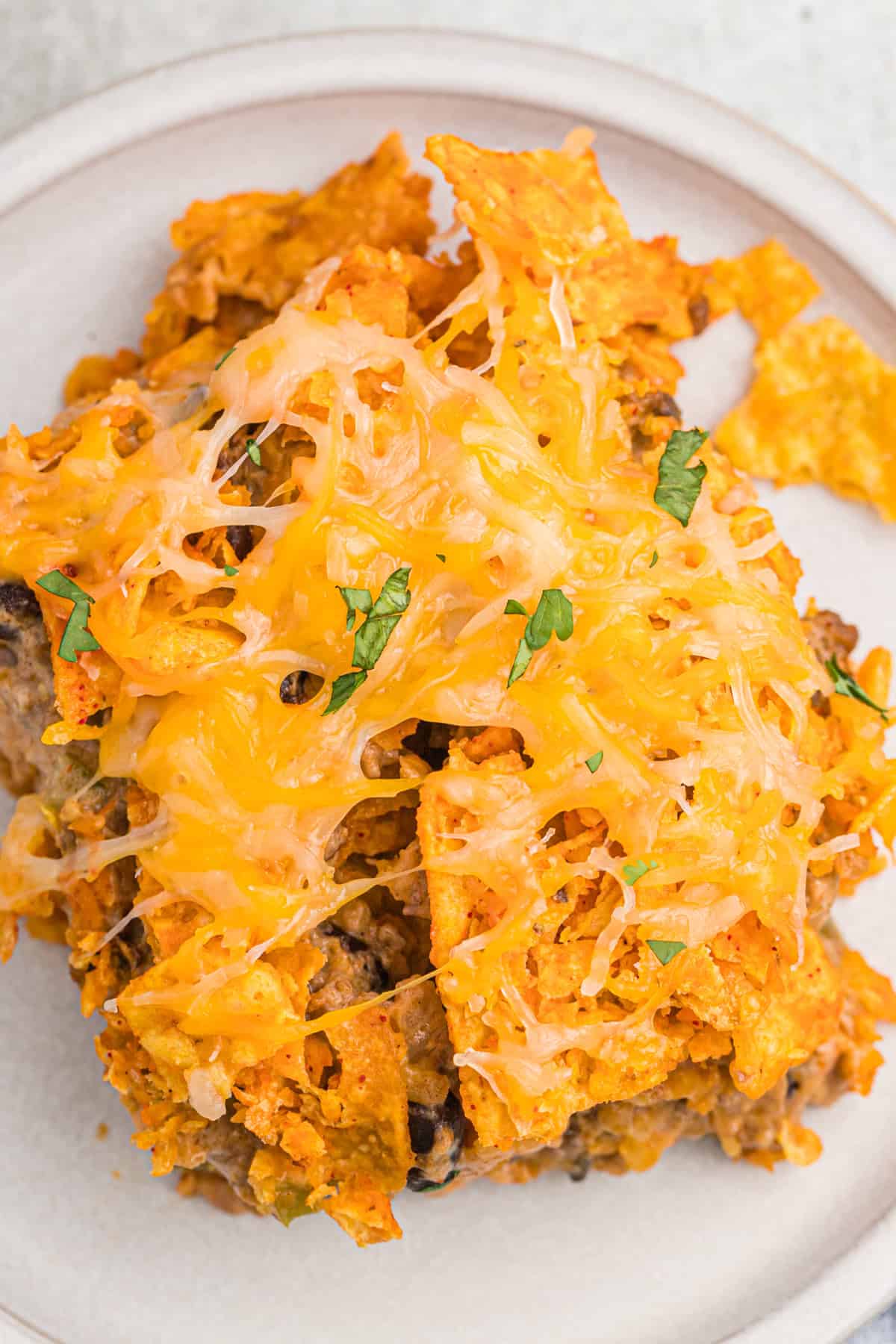 A closeup of Dorito casserole on a plate, topped with melted cheese and garnished with herbs