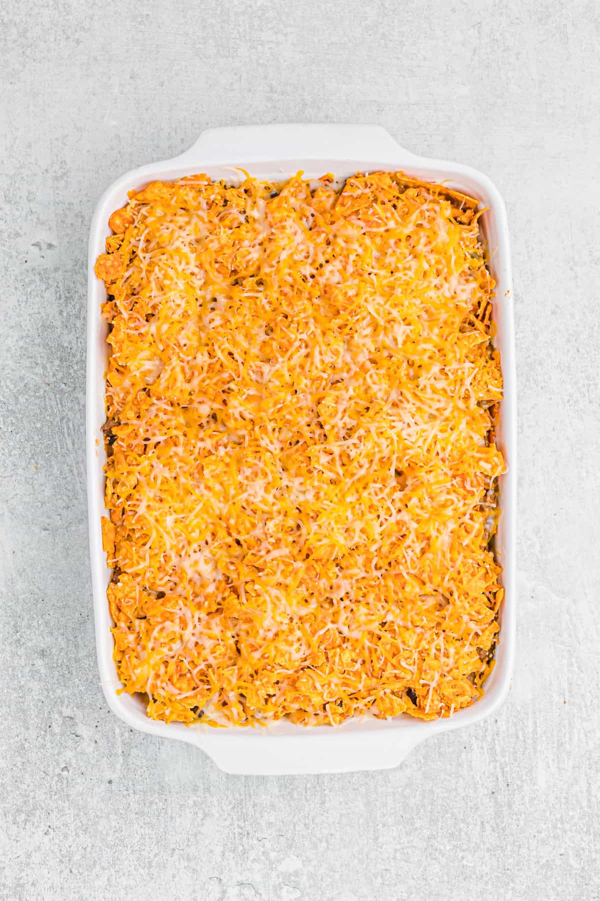 A casserole dish filled with a baked Dorito casserole, topped with melted cheese