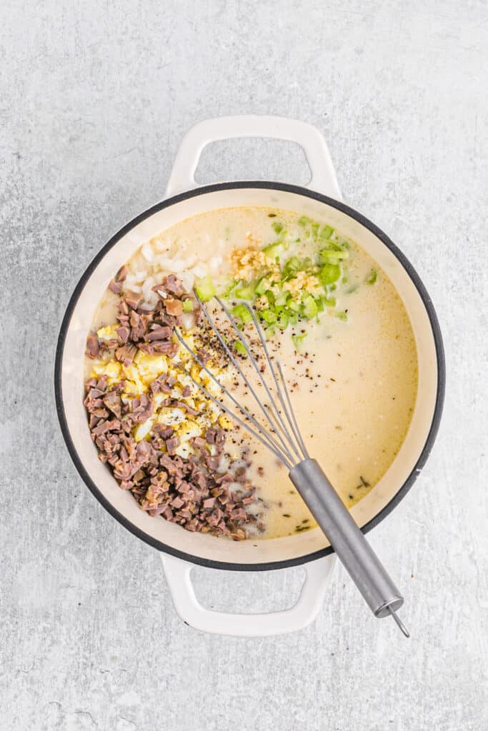 Giblets, egg, celery, onion, garlic and salt and pepper added to a pot of gravy on gray countertop