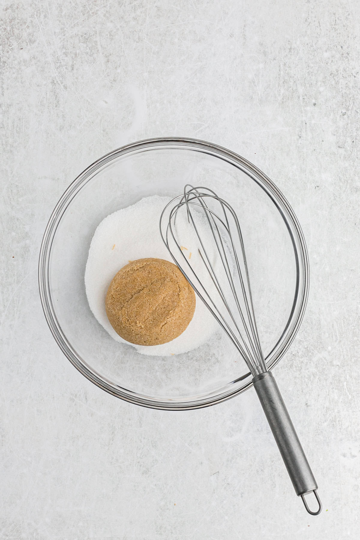 Brown sugar and granulated sugar in a glass bowl with a whisk on white countertop