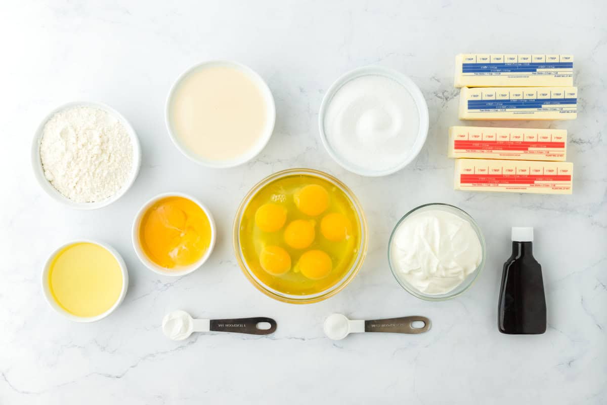 Eggs, sugar, flour, butter, vanilla and other ingredients on a white surface in bowls and measuring spoons to make a Southern caramel cake
