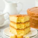 A slice of old fashioned caramel cake on a white plate with a fork full taken out on a white background