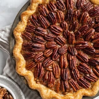 A perfect pecan pie recipe on a white background with a bowl of pecans nearby under a napkin