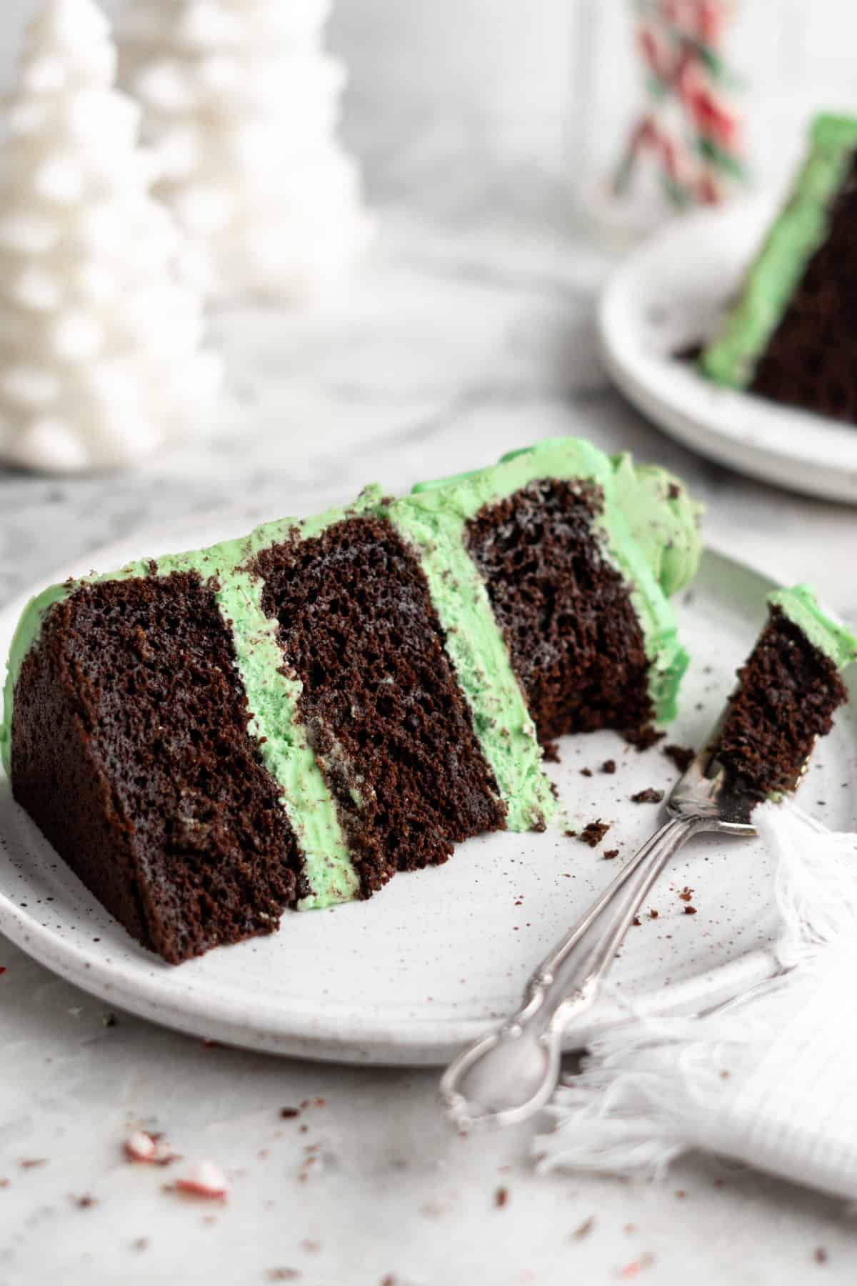 A slice of mint chocolate cake with green frosting served on a white plate, with a fork and festive crumbs scattered around