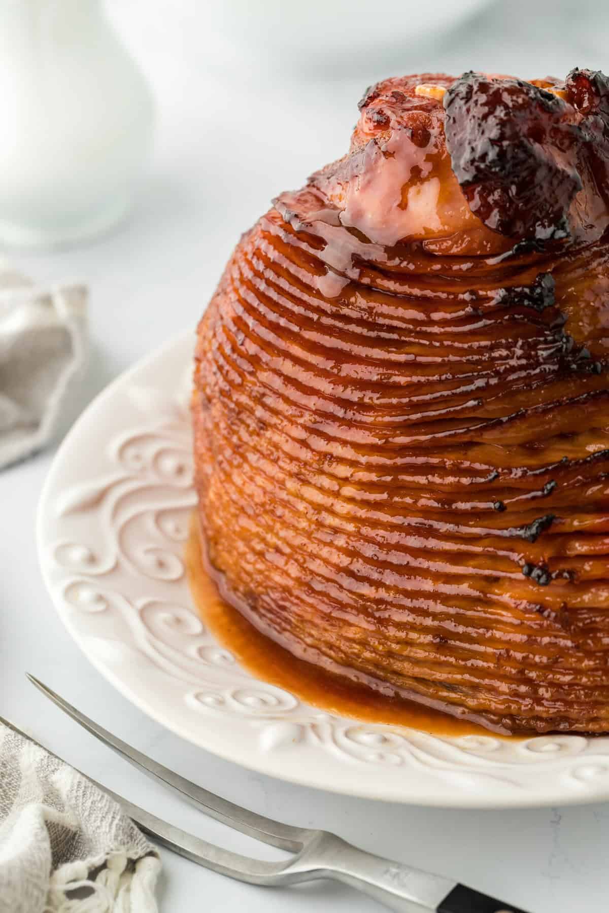 A honey glazed ham on a white platter in white background