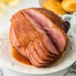 Honey glazed ham on white platter ready to serve with bread in background