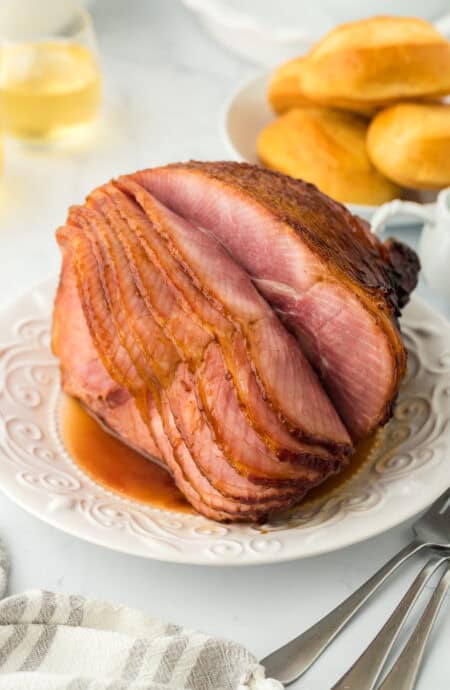 Honey glazed ham on white platter ready to serve with bread in background