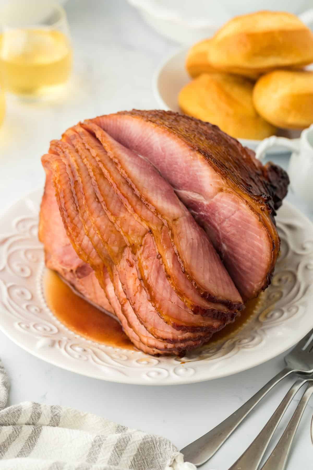 Honey glazed ham on white platter ready to serve with bread in background