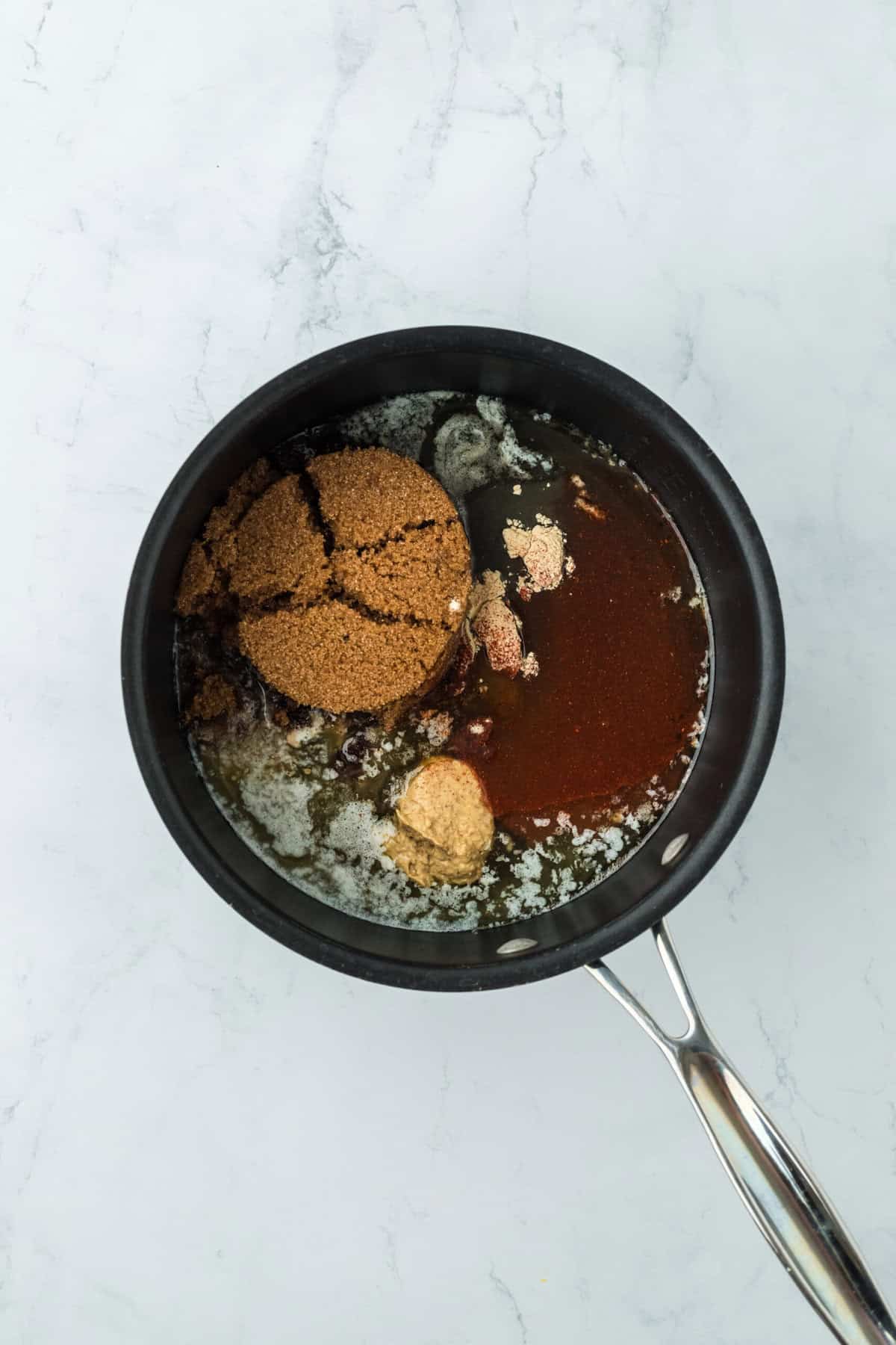 Brown sugar and honey and spices in a pot to make a glaze on white countertop