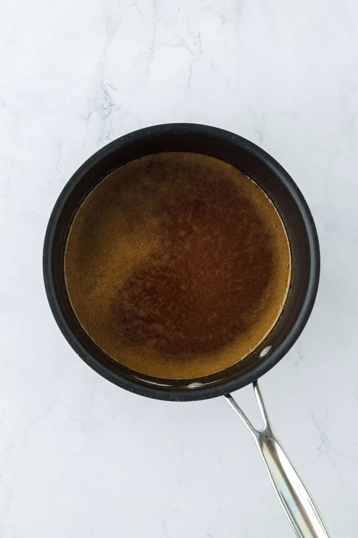 Ham glaze in pot being thickened and cooked down on white countertop