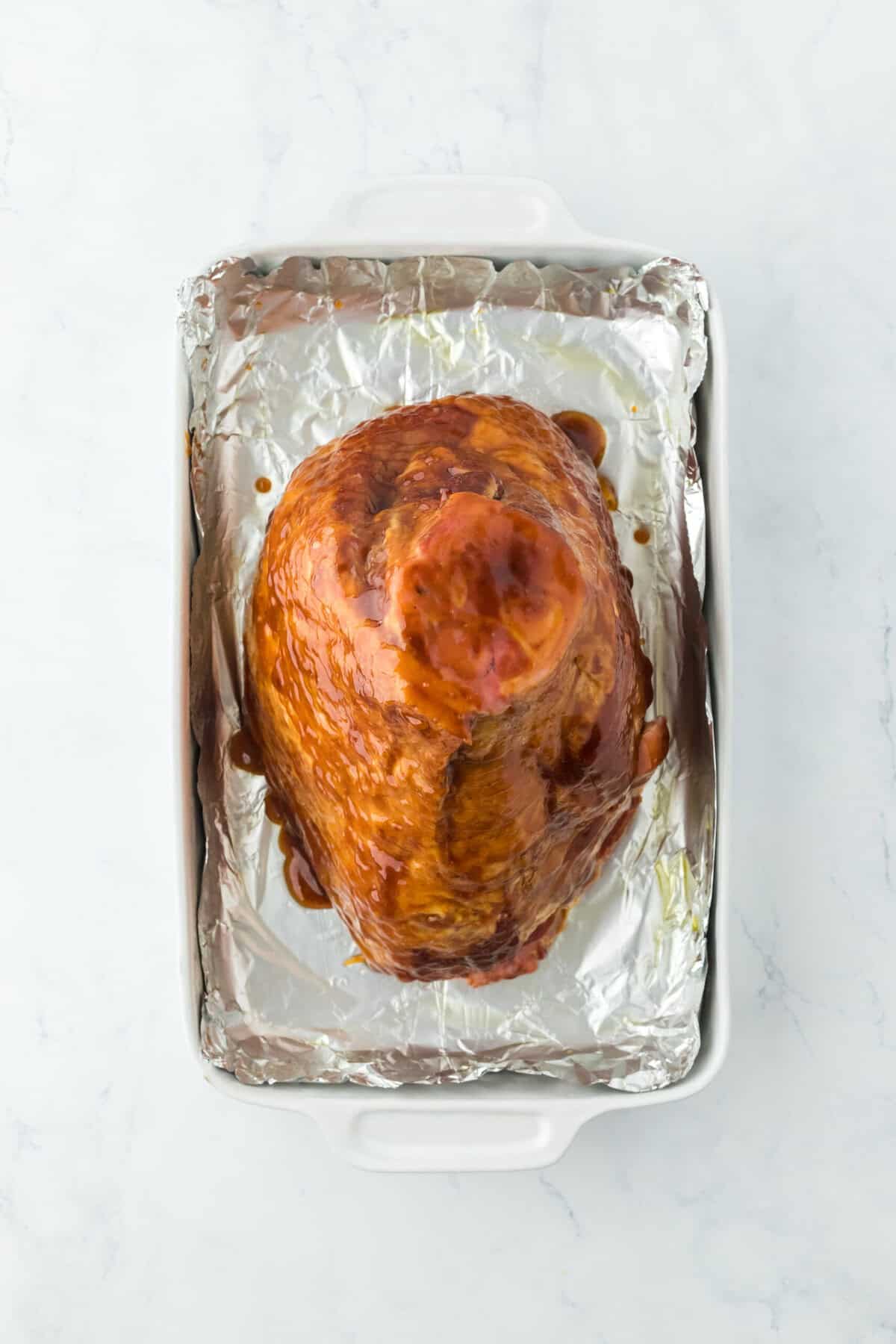 Spiraled ham on a foil lined baking sheet on white countertop