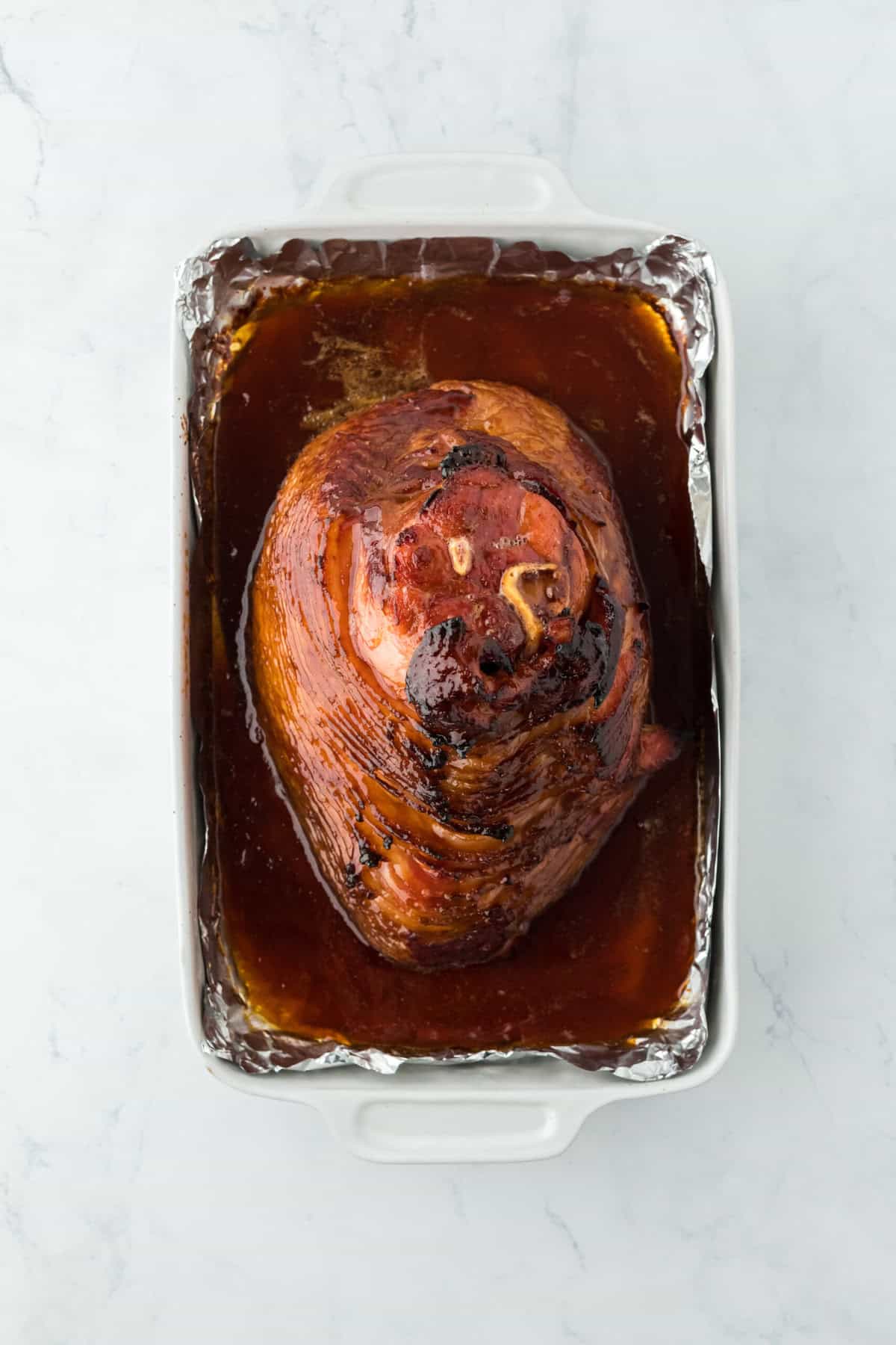 Honey glazed ham after being baked on a foil lined baking sheet on white countertop