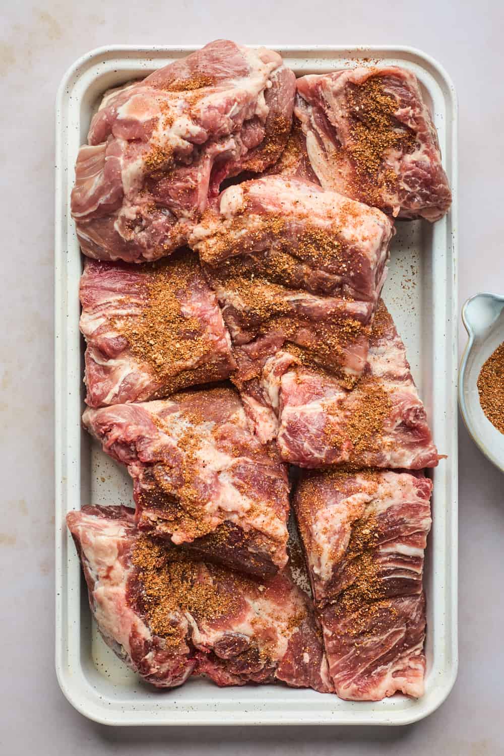 Pork necks on a baking sheet with spices ready to rub into them.