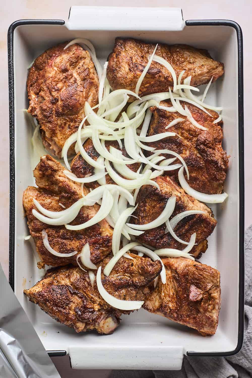 Sliced onions over browned pork neck bones in a baking dish.