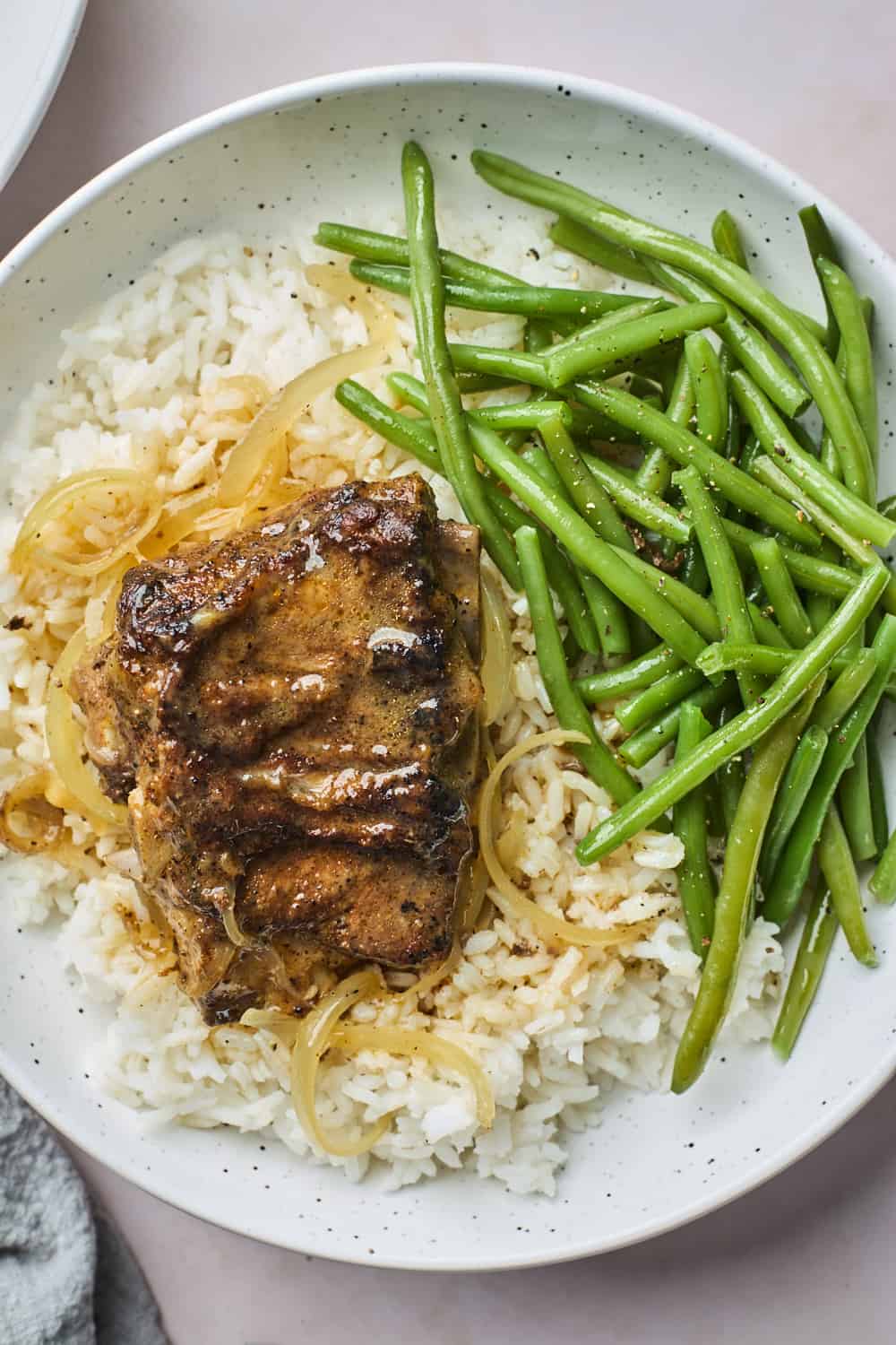 Roasted pork neckbones over rice next to green beans on a plate.