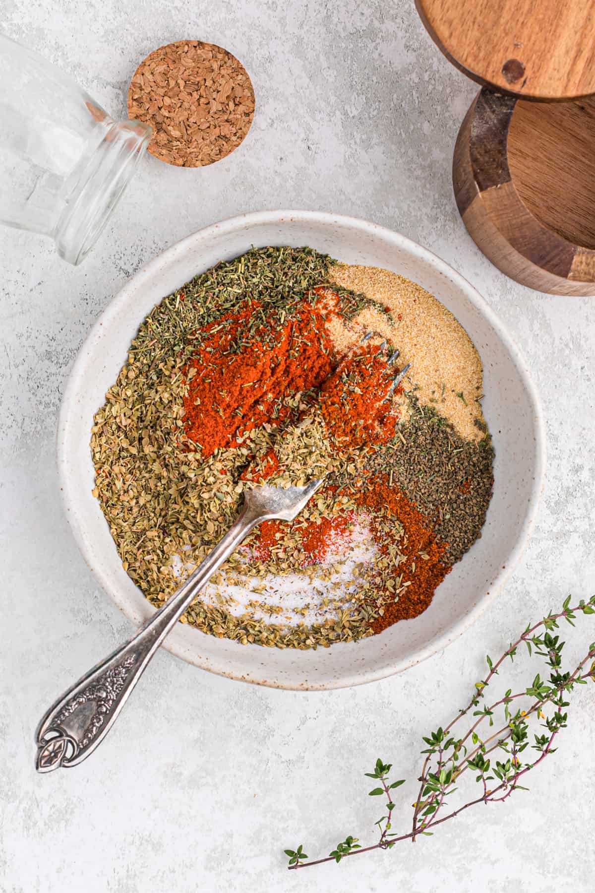 A fork mixing up a bunch of seasonings in a flat white bowl.