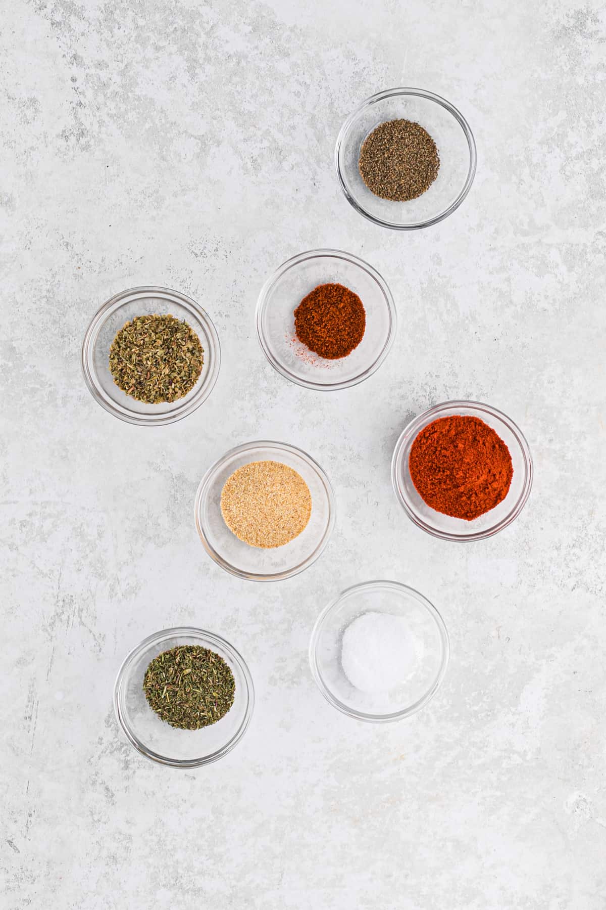 Individual spices in small glass bowls on a white surface.