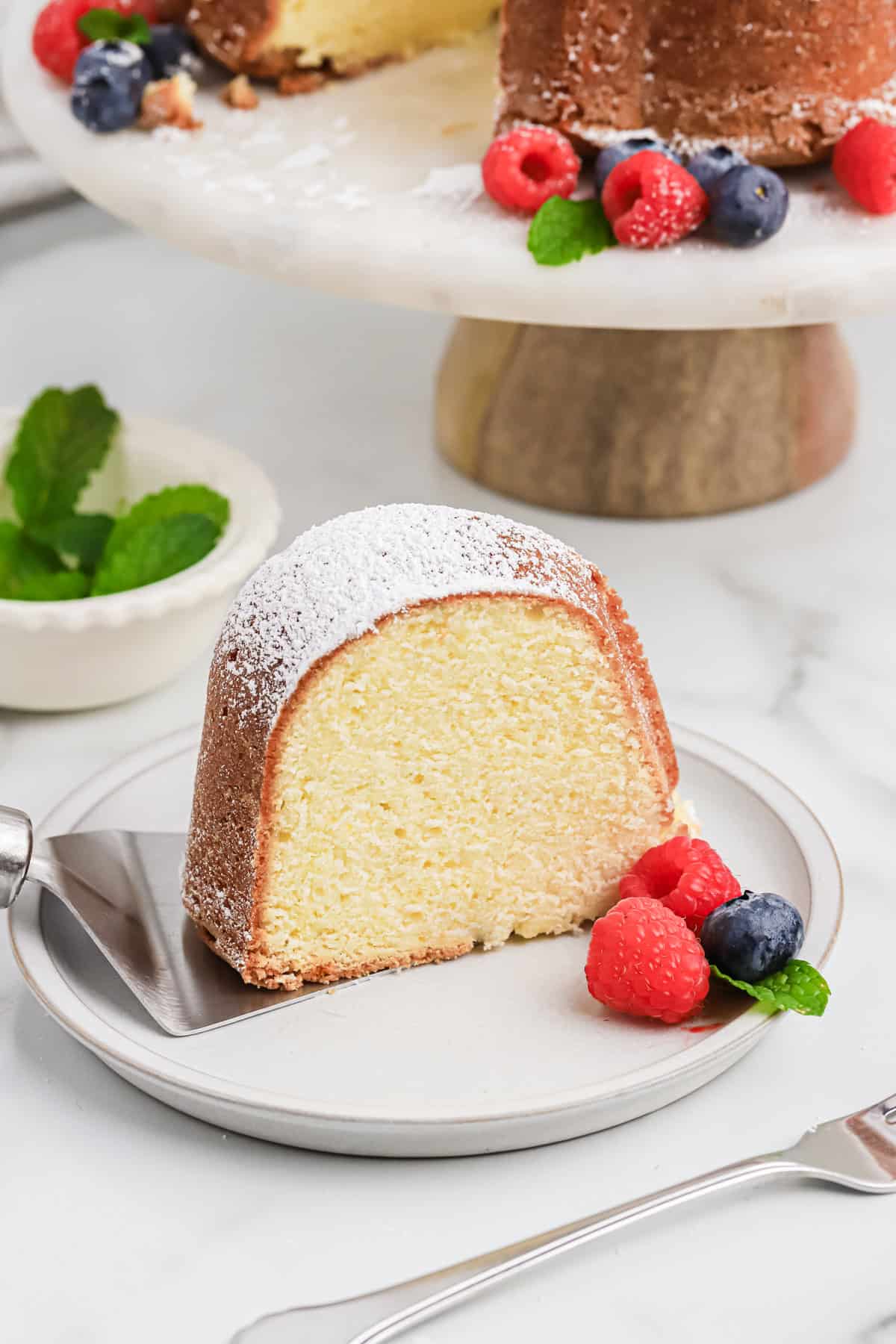 A slice of cream cheese cake on a white plate with berries next to it