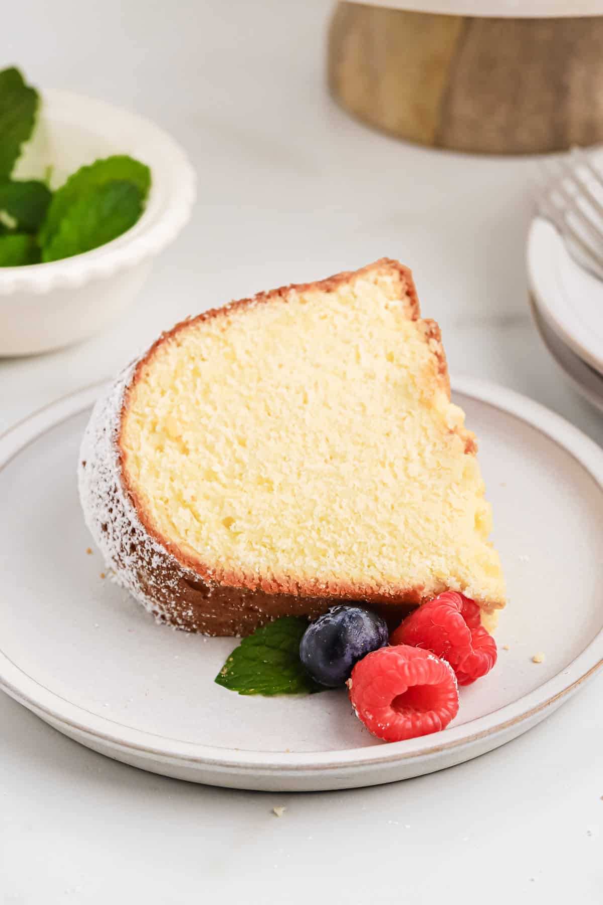 A slice of cream cheese pound cake recipe laying down on a white plate with berries on it on white background