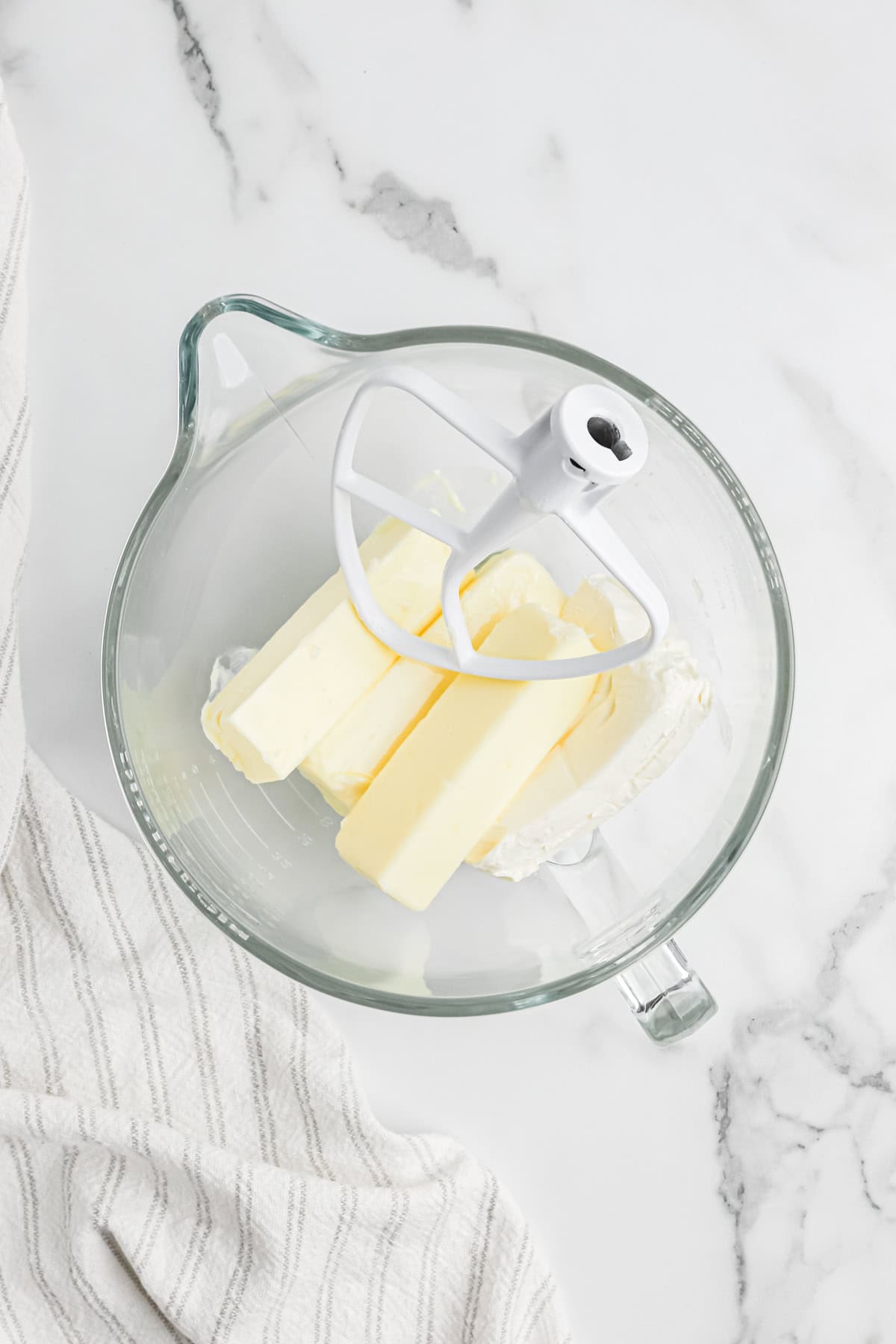 Butter, oil and cream cheese added to a clear stand mixer bowl on white background