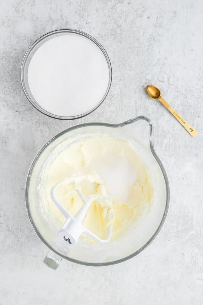 Sugar added to the beaten butter in a mixer bowl on white background