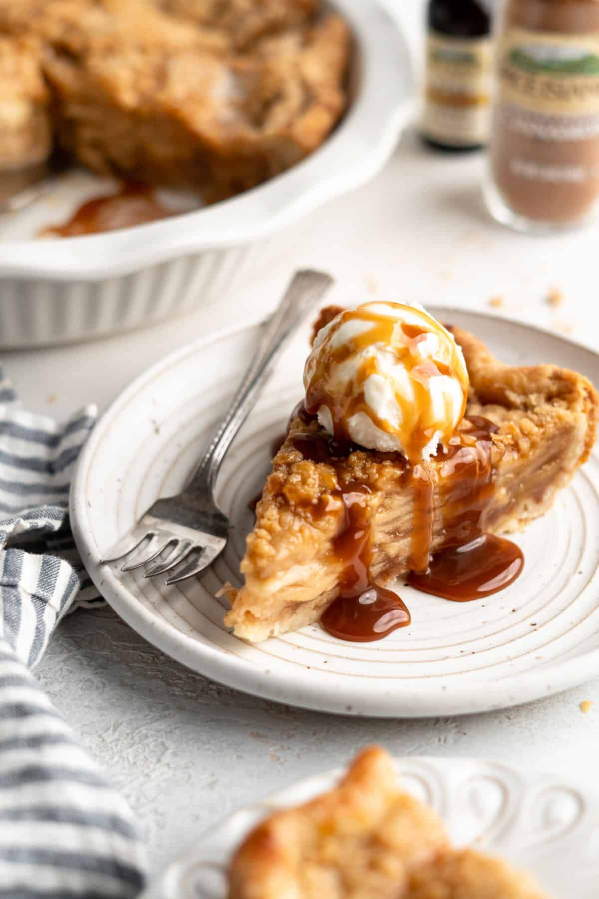 A slice of apple pie with caramel sauce and ice cream on top served on a white plate