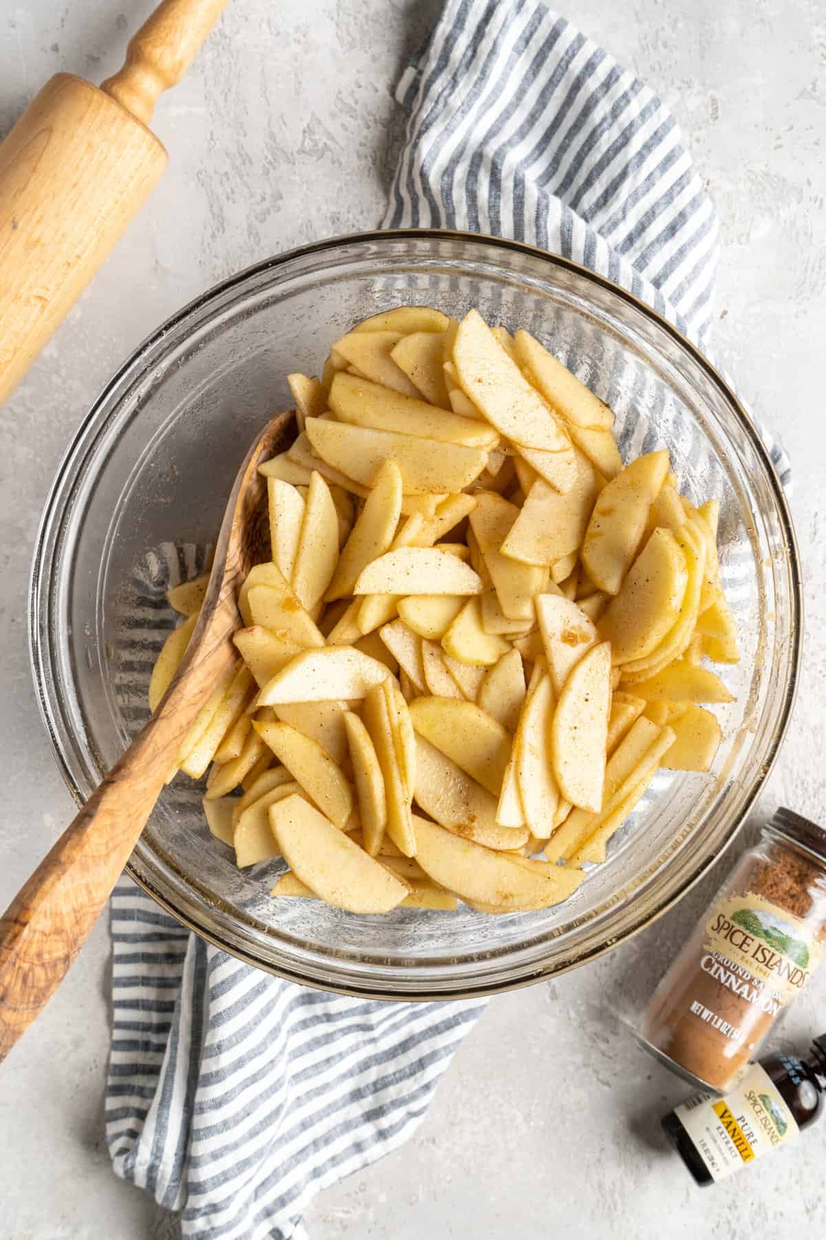 Slices of apple in a clear bowl with a wooden spoon