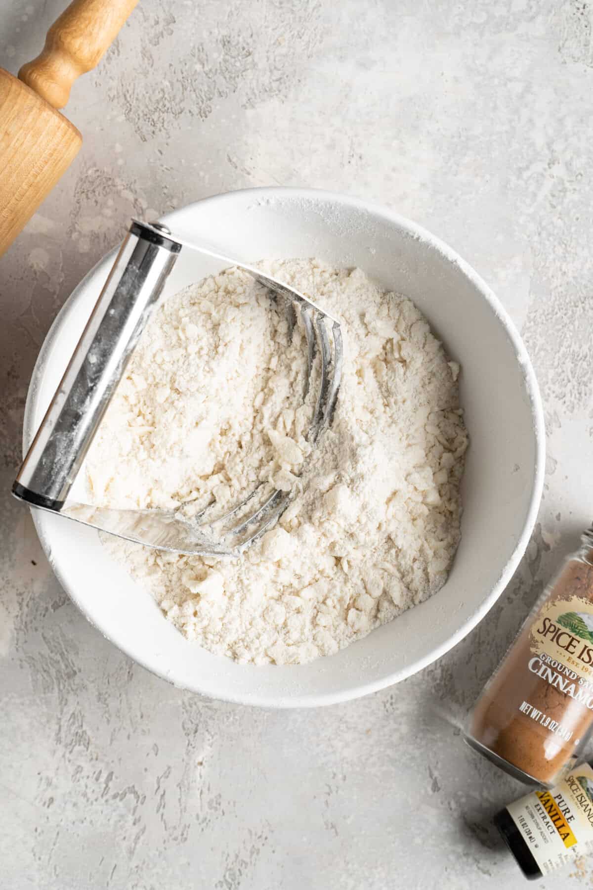 Butter being cut into flour mixture in a white mixing bowl.