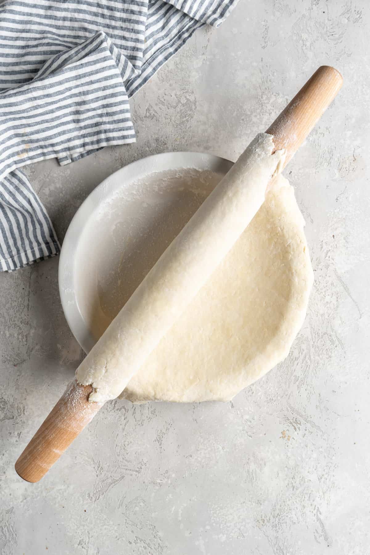 Pie dough around a rolling pin being added to a pie plate