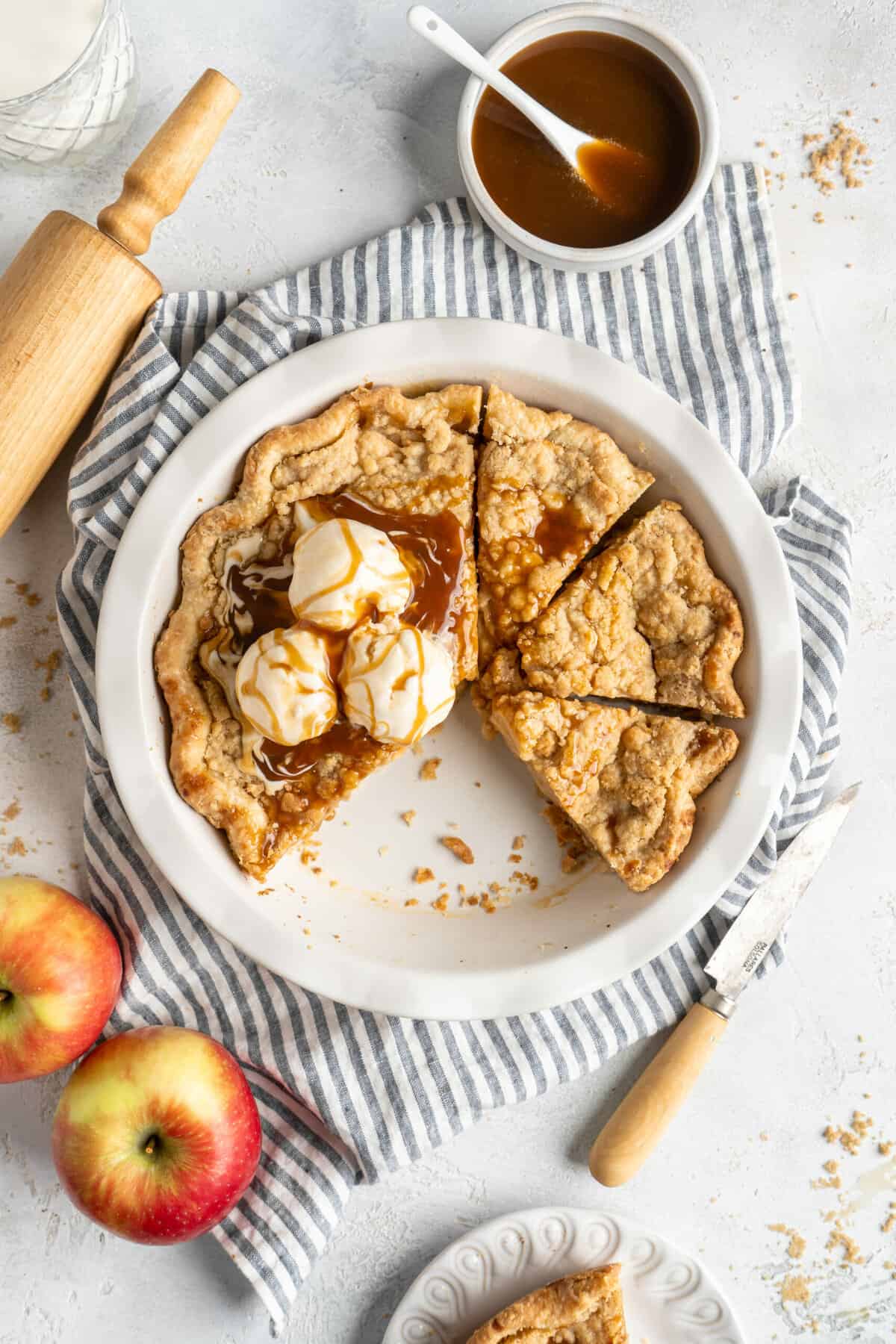 Dutch apple pie slices ready to serve with ice cream on top of a white countertop with spiced caramel nearby.