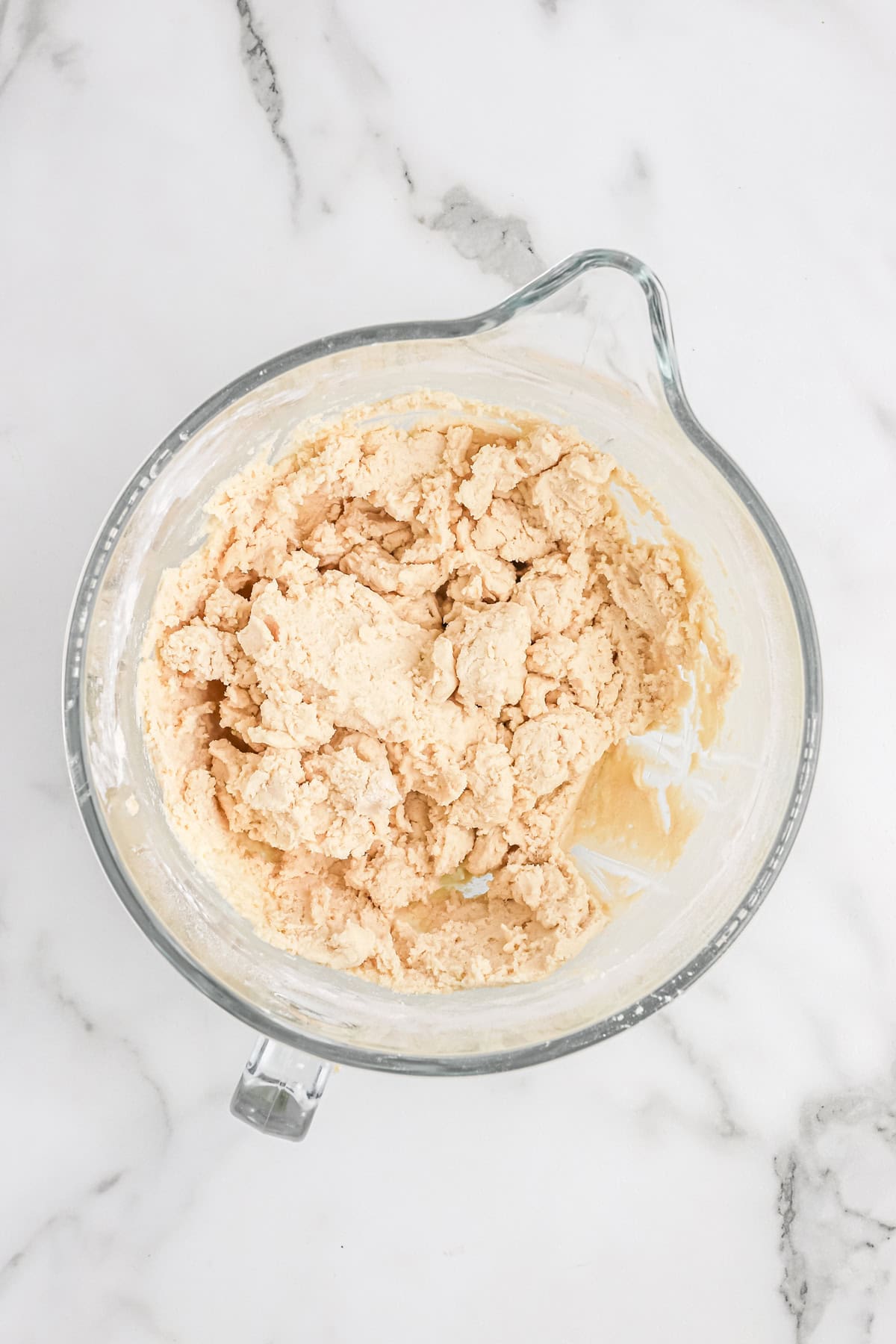 A glass bowl showing the sugar cookie dough mixed and crumbly, ready to be shaped and chilled