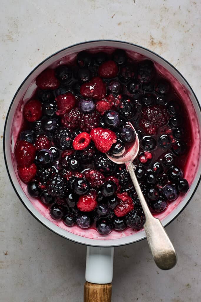 Berry compote and a silver spoon in a white saucepan.