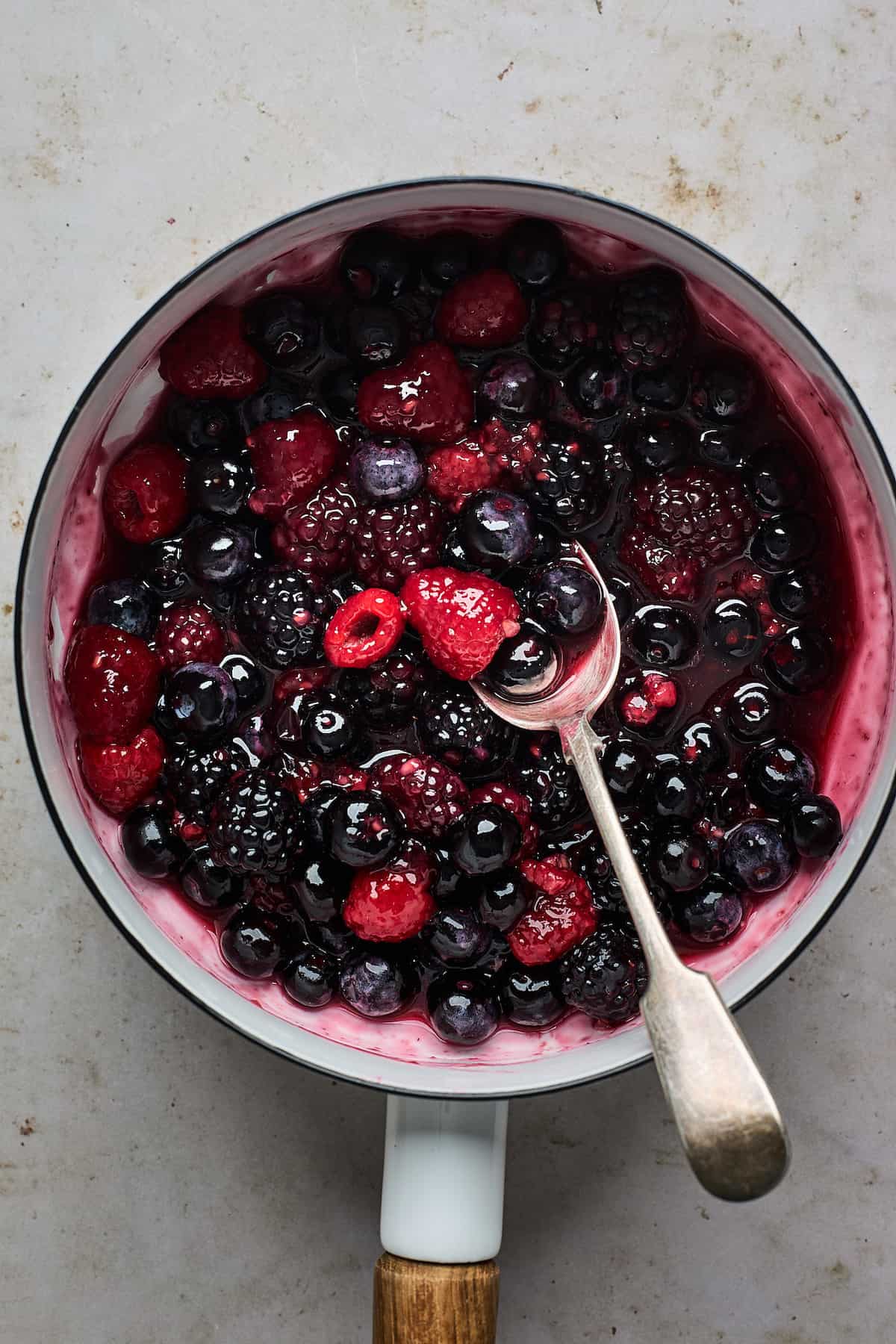 Berry compote and a silver spoon in a white saucepan.