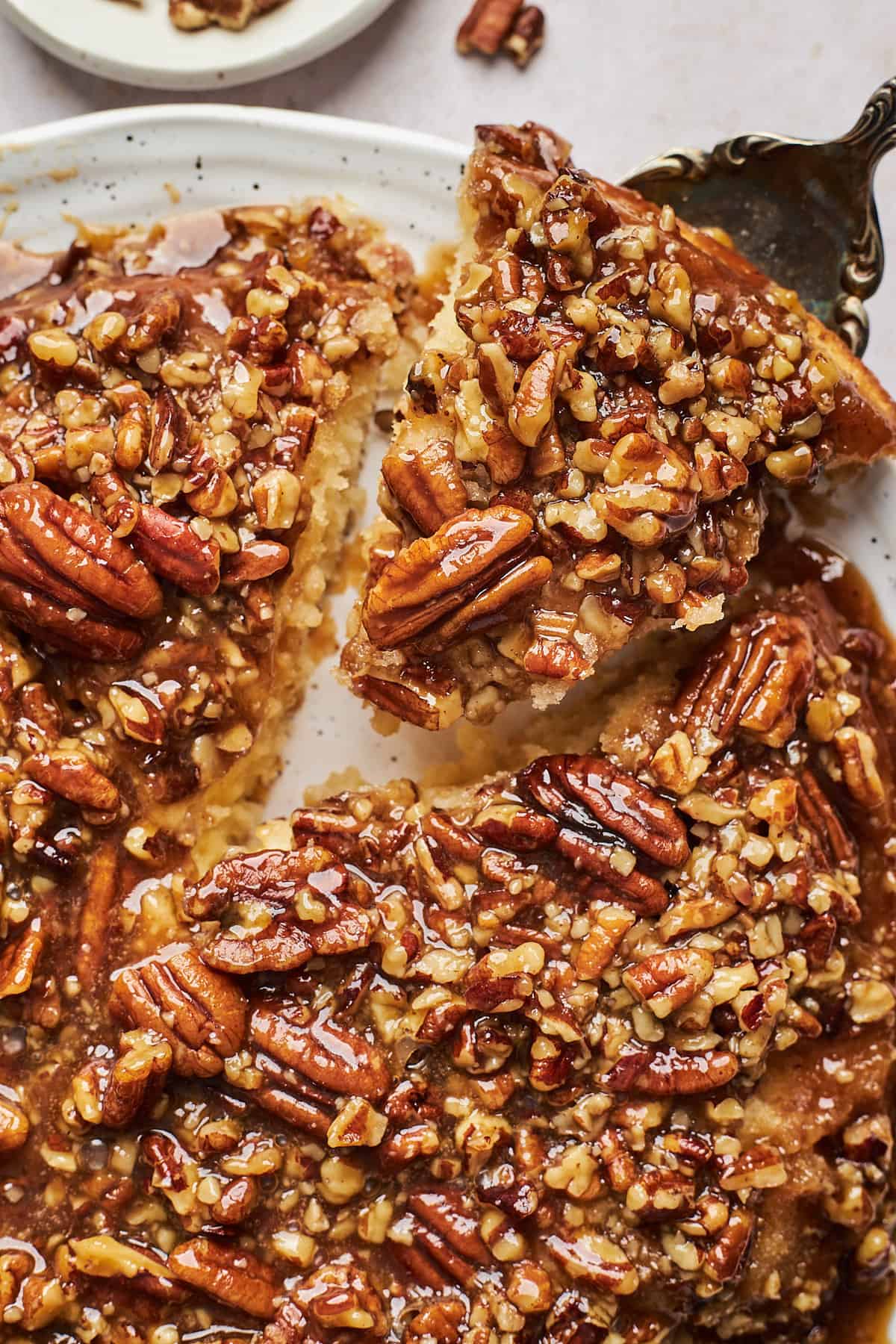 a slice of cake being taken out of the whole pecan pie cake