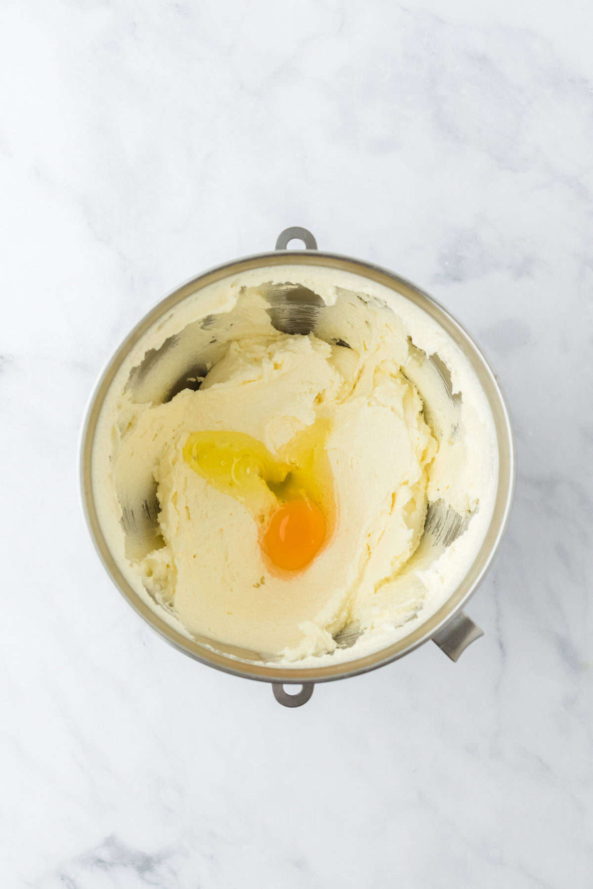 Add eggs to stand mixer for creamed butter and sugar on white countertop