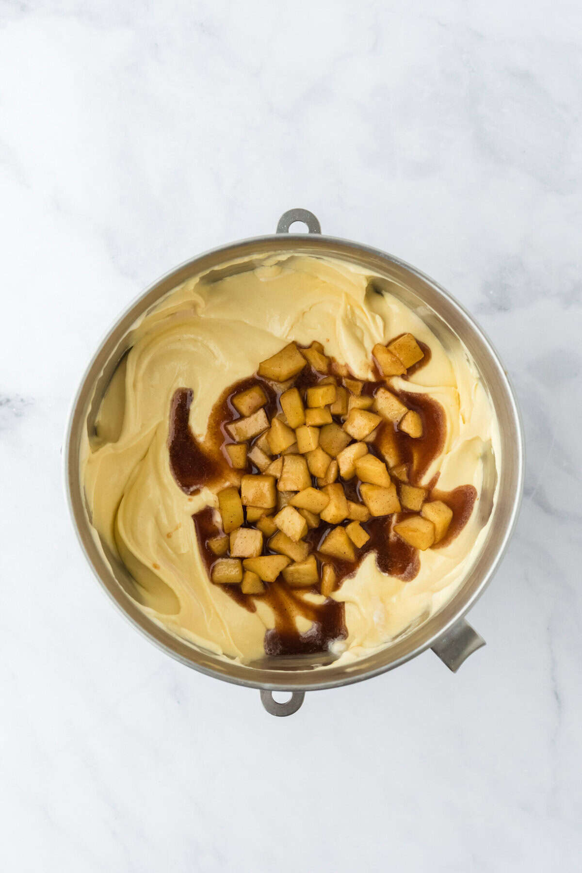 Apple filling added to cake batter in stand mixer bowl on white countertop