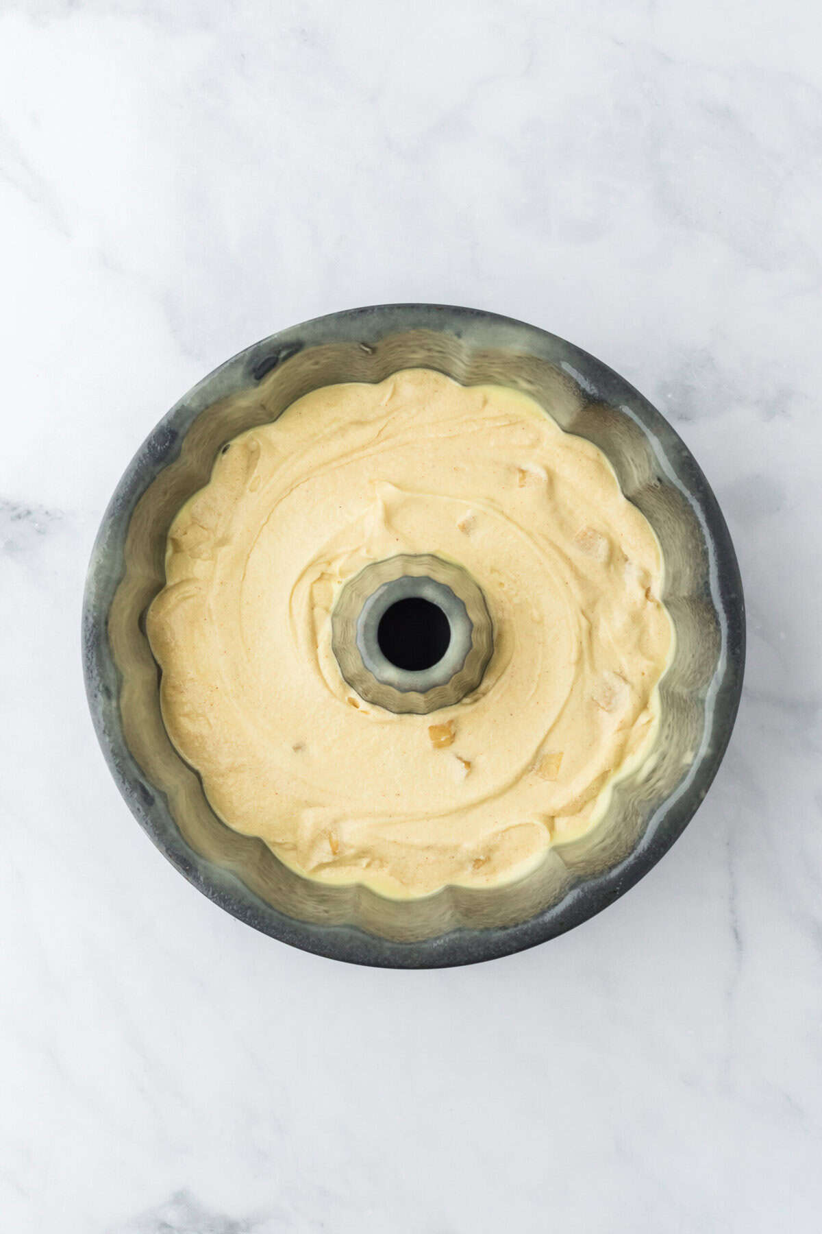 Half of caramel apple bundt cake batter poured into greased bundt pan on white countertop