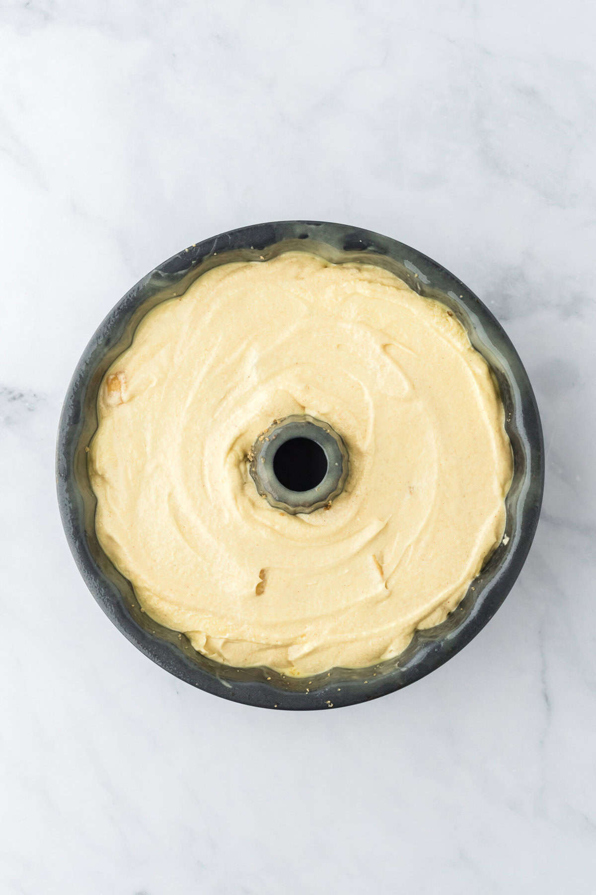 Bundt pan filled with cake batter on white countertop before baking