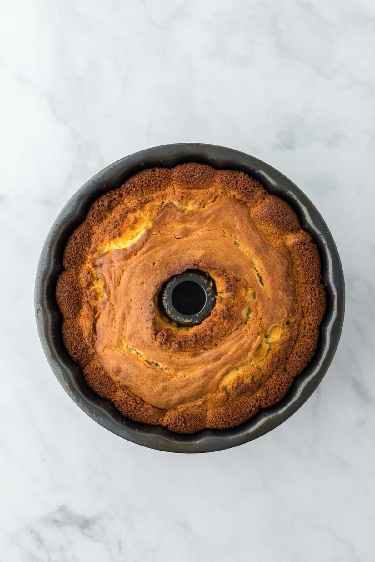 Baked pound cake in bundt pan out of the oven on white countertop