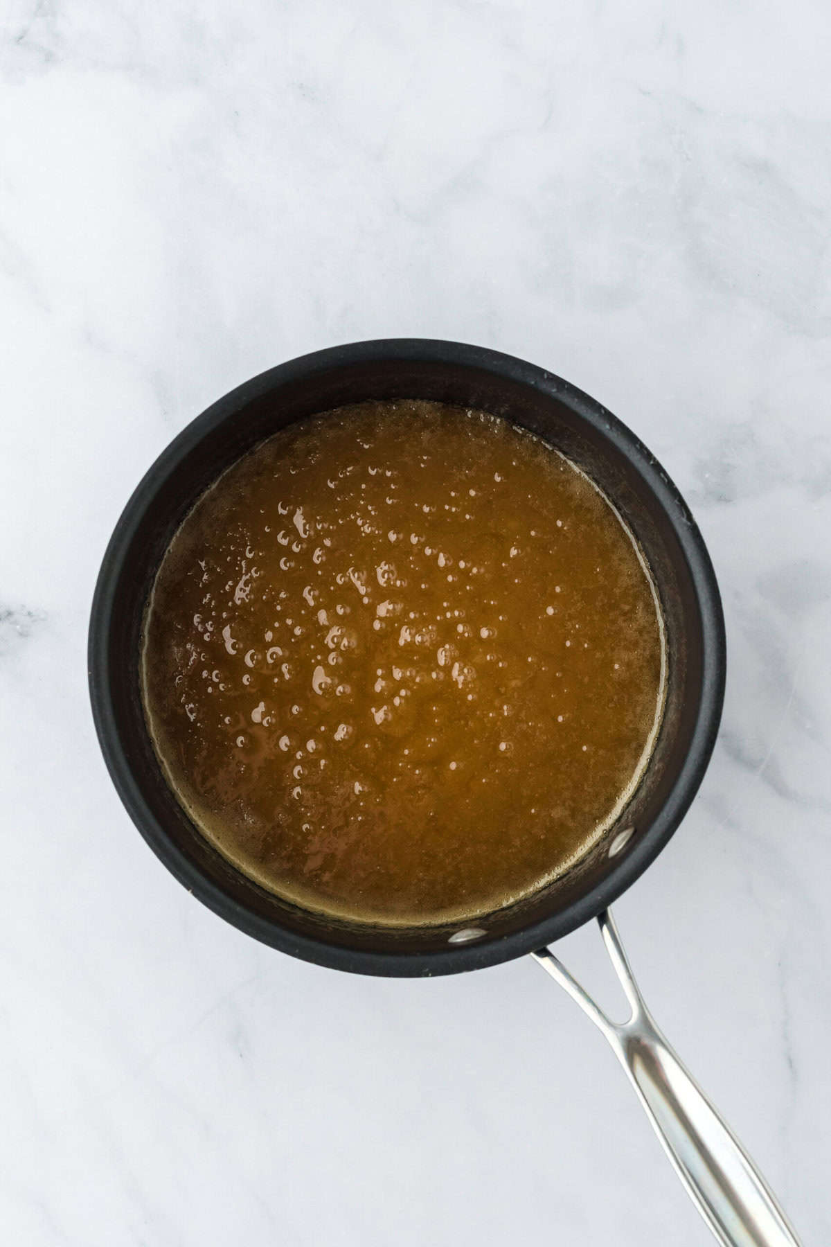 Caramel sauce boiling in a saucepan on white countertop