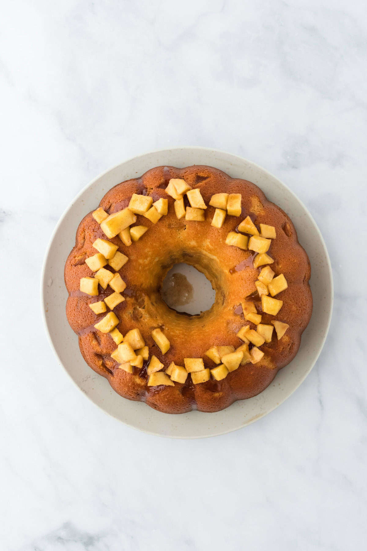 An overhead of an apple cake with apple chunks on top on white countertop