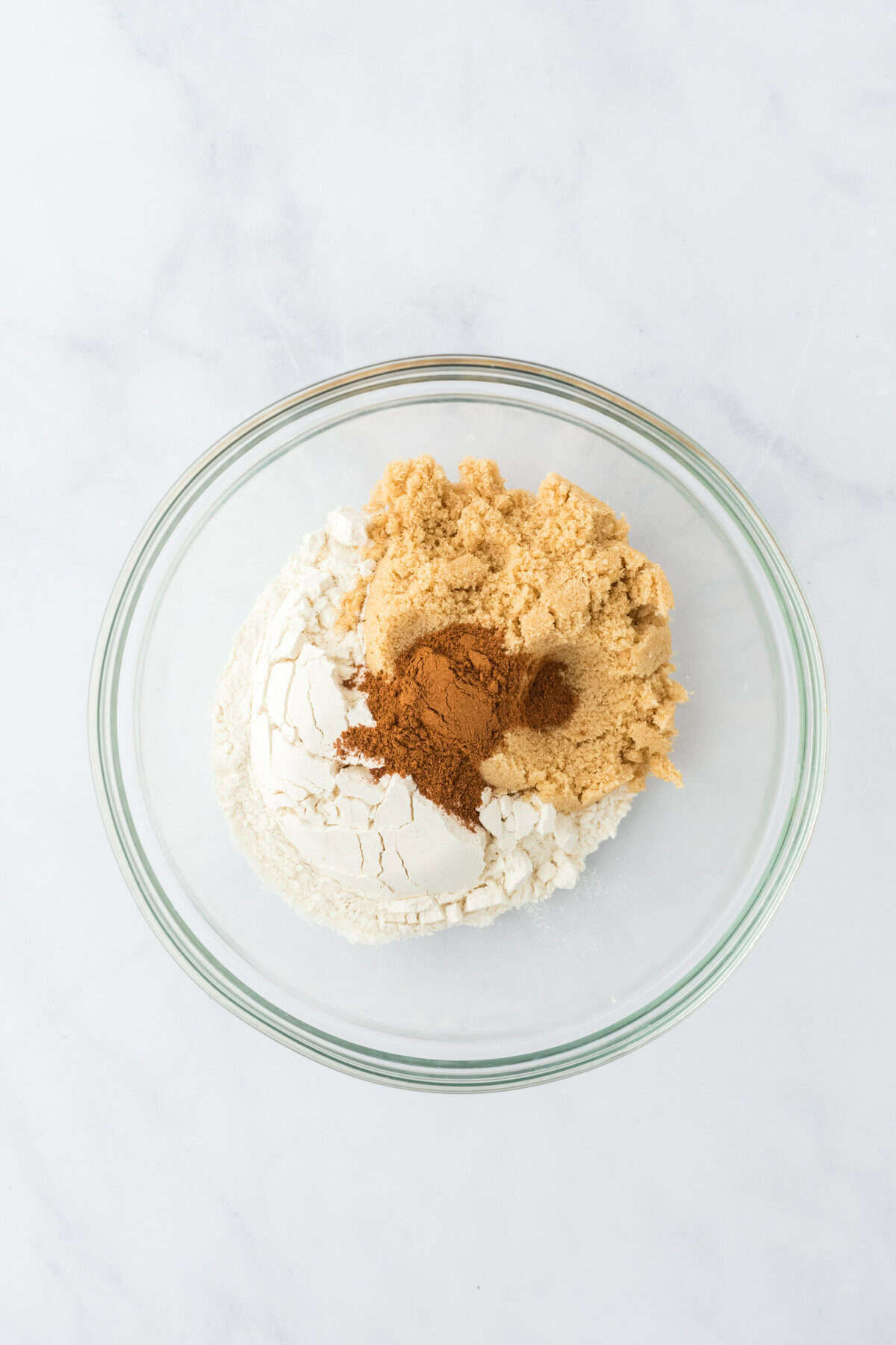 Flour, brown sugar and spices in a glass bowl on white countertop