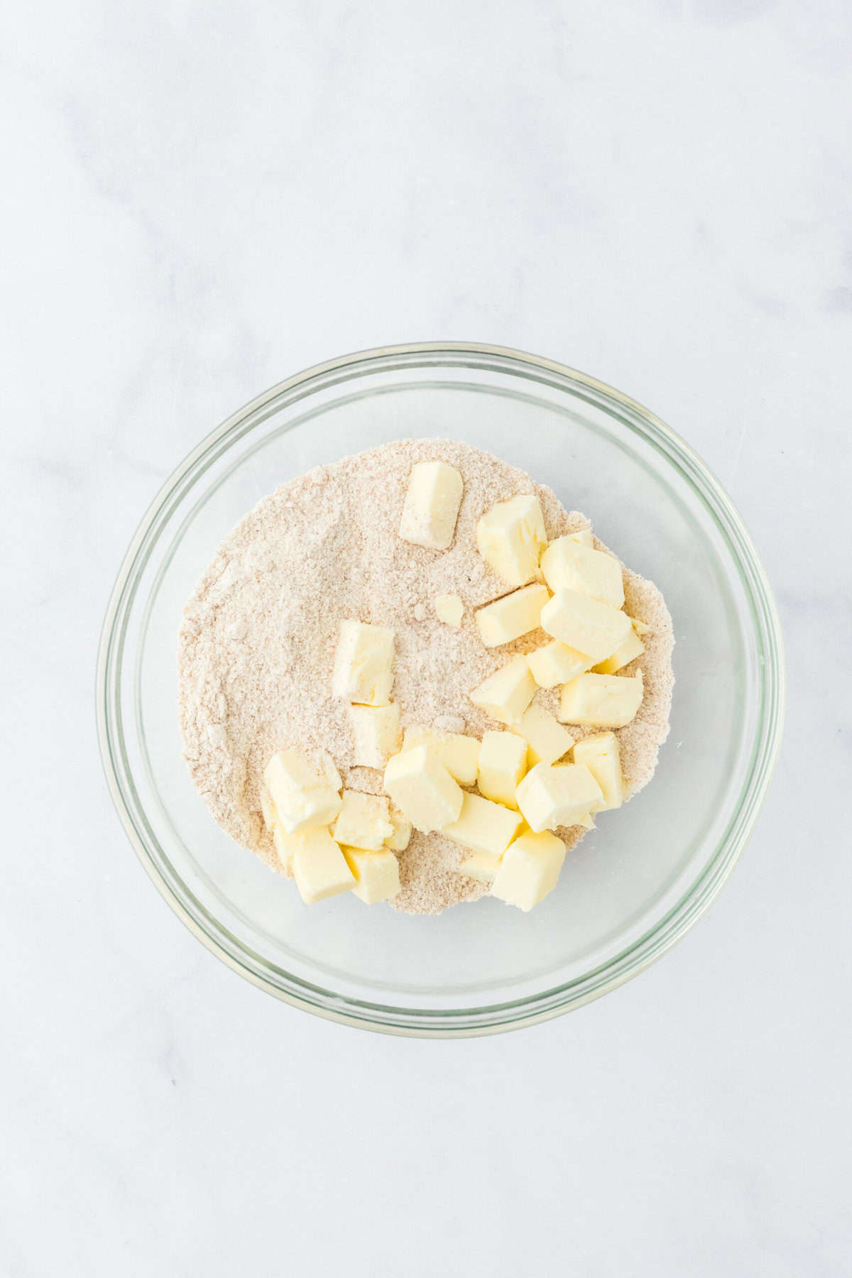 Cold butter cubes in a brown sugar spiced dry ingredient bowl on white countertop