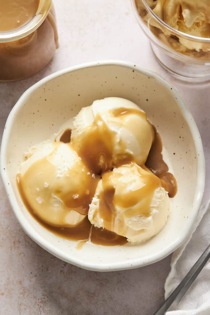 three scoops of ice cream in a bowl covered with caramel sauce