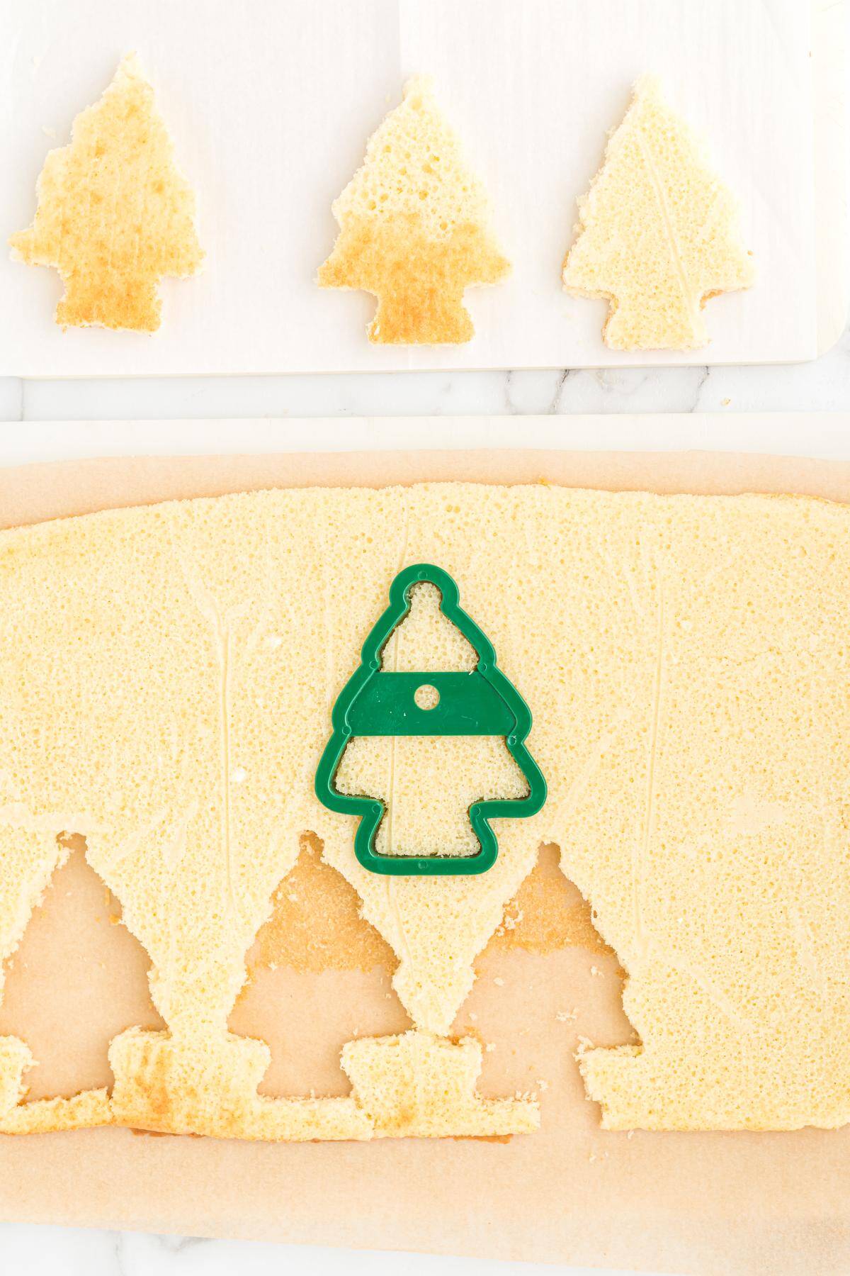 A green Christmas tree cookie cutter pressed into the sheet cake with cut-out tree shapes above it