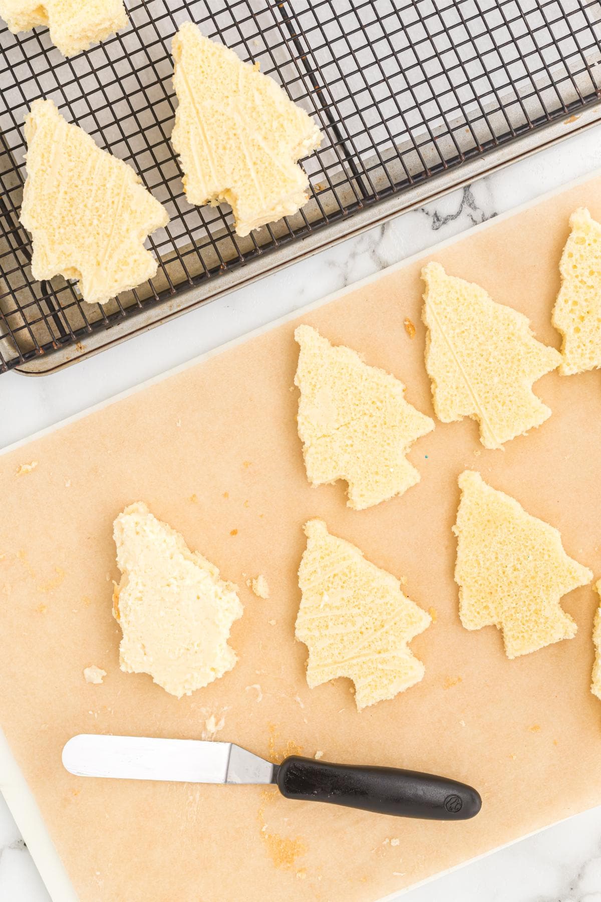 Several Christmas tree cake cutouts arranged on a rack and a cutting board, with an offset spatula nearby