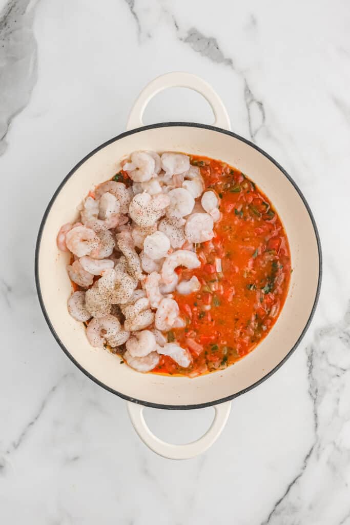 Raw seasoned shrimp being added to a creole tomato sauce base